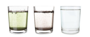 Drei Gläser voll Wasser mit jeweils unterschiedlichem Verschmutzungsgrad des Wassers 
