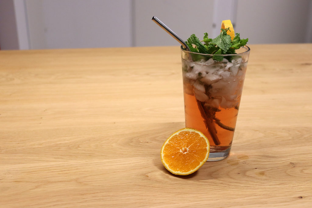 Sommergetränk mit Tom Brolin in einem hohen Glas, verziert mit Minze und Orangen
